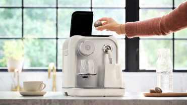 A person places a compressed coffee tablet inside a Keurig Alta machine sitting on a counter.