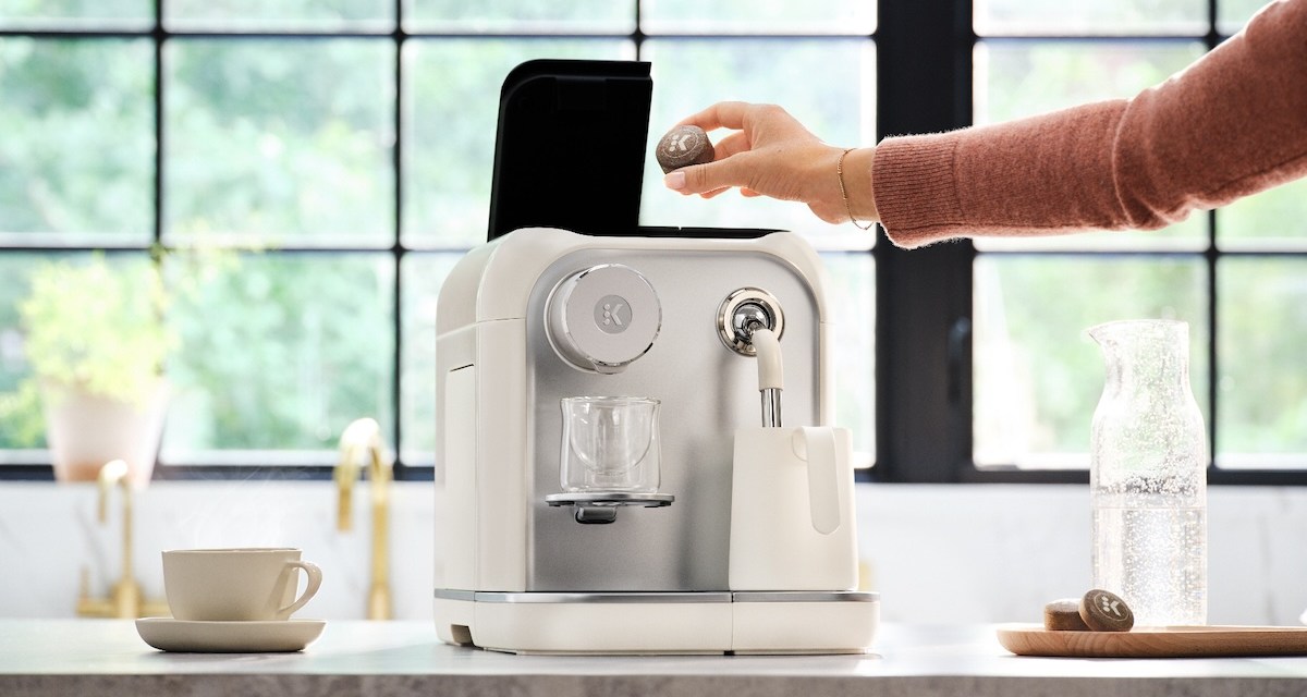 A person places a compressed coffee tablet inside a Keurig Alta machine sitting on a counter.